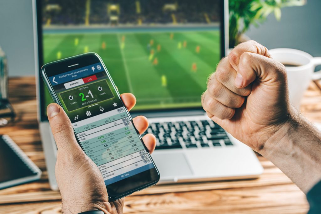 Man watching football on a laptop whilst sports betting on his mobile