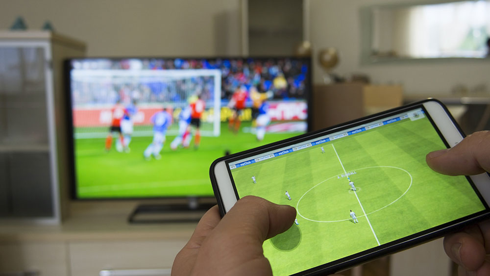 Sports journalism is evolving. This image shows someone streaming a game on a tablet while also watching on a TV